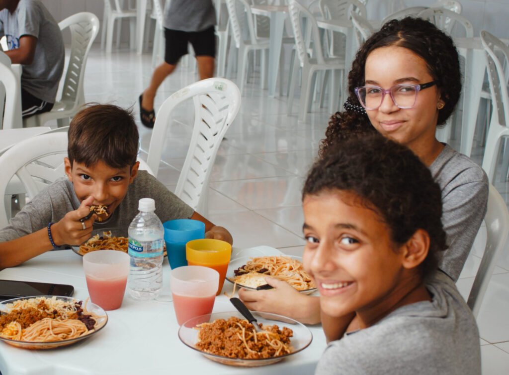 Children sitting around table eating spaghetti at FAD community center