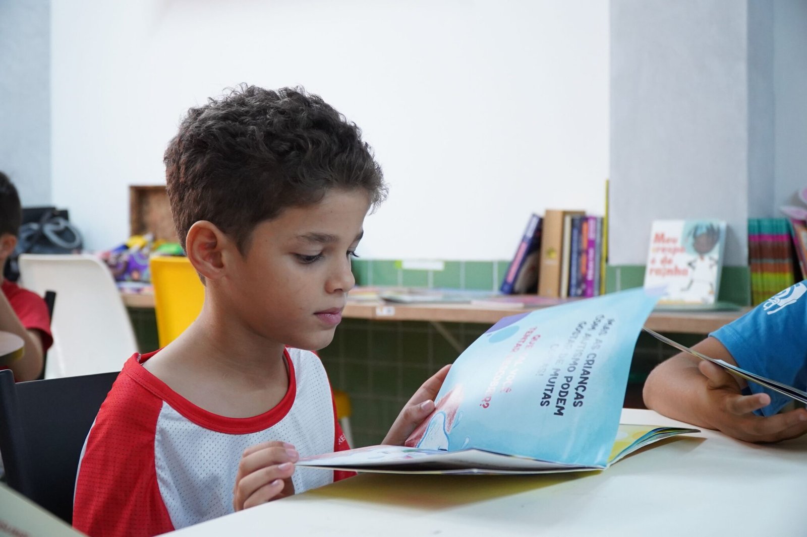 Boy reading a book in a red shirt at FAD community center in Brazil