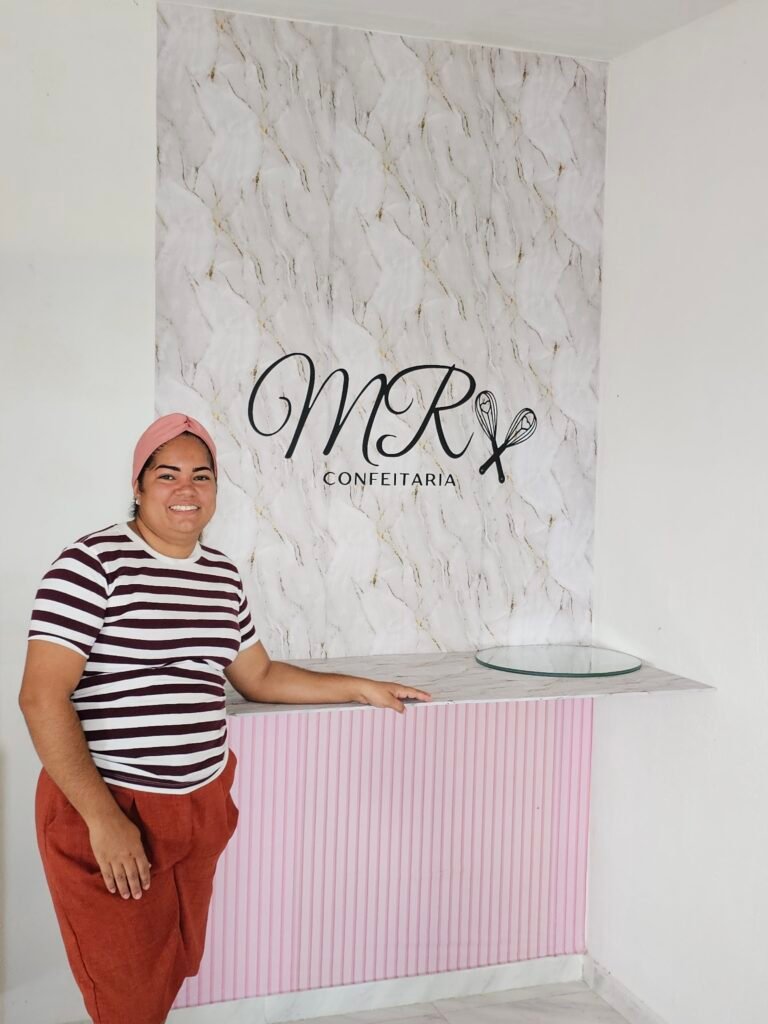 Woman in striped top smiling in front of a bakery sign that says MR Confeitaria 