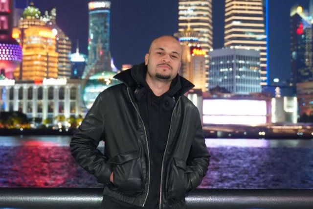 Young man in black jacket posing in front of water and skyline