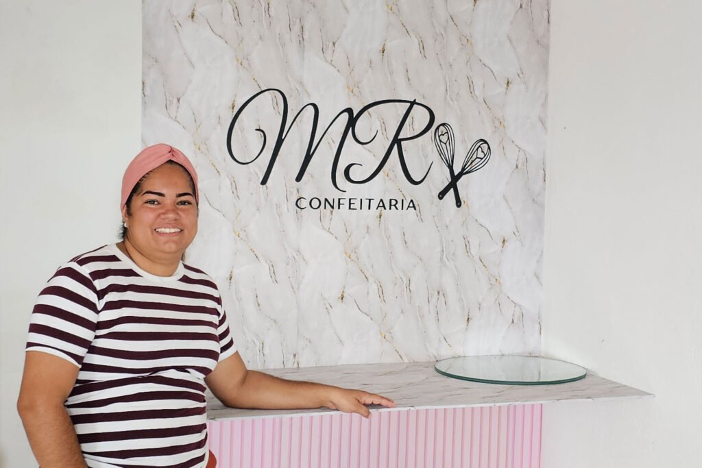 Woman in striped top smiling in front of a bakery sign that says MR Confeitaria